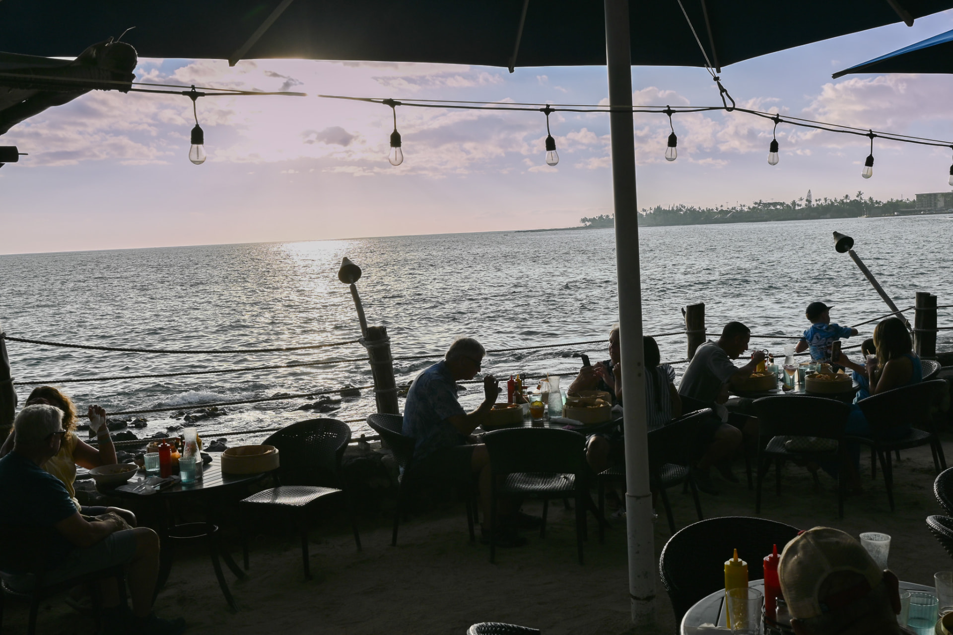 Guests dining on the sand as the sun sets over the water in Kailua-Kona