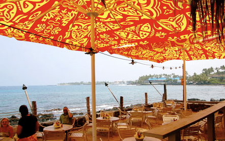 Beachside dining area with a large red and yellow patterned umbrella overlooking the ocean